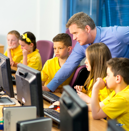 
Na zdjęciu widzimy grupę dzieci w żółtych koszulkach, siedzących przy komputerach w sali informatycznej. Uczniowie wyglądają na skupionych na ekranach monitorów, co sugeruje, że są zaangażowani w naukę lub zadanie związane z technologią.